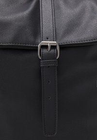 Zwarte leren tas met een glad oppervlak, rechthoekige vorm, zilveren metalen gesp en een strap met verstelbare gaten.