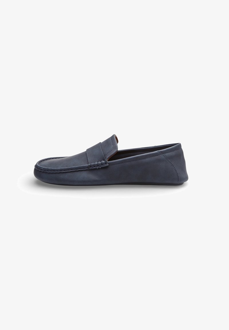 Mocasín de ante azul marino sin cordones con costuras moc toe y tacón bajo, mostrado de perfil sobre fondo blanco.