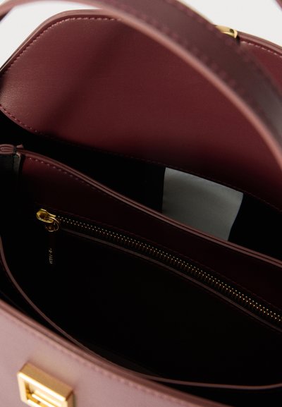 Otevřená bordová kožená kabelka se zlatým zipem a částečným pohledem na bílou látku uvnitř.
