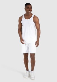 Ensemble en coton blanc composé d'un débardeur et d'un short, présentant une texture lisse, un col rond et une coupe décontractée, accompagné de chaussures de sport blanches.