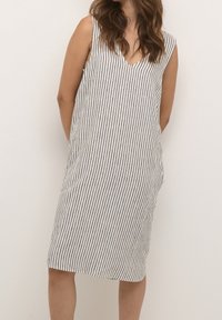 Vestido sin mangas con escote en V, hecho de una tela ligera con rayas verticales en blanco y negro, de longitud hasta la rodilla y con un corte holgado.