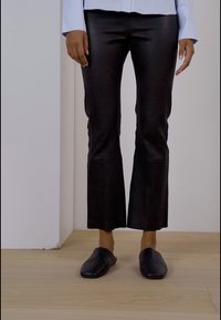 Sorte faux læder flared bukser med en glat overflade, der har en let glans. Støttet med sorte slip-on sko.