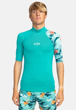 Türkiser Rashguard mit kurzen Ärmeln und floral gemusterten Schultern; weicher, dehnbarer Stoff; weißes Logo auf der Brust; enganliegendes Design; glatte Textur.