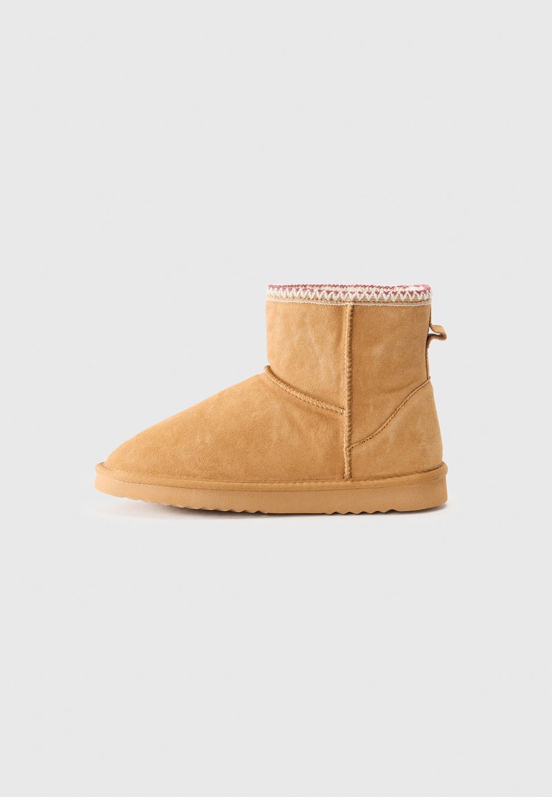 Bottes de cheville en suede beige avec un bout arrondi, une bordure tricotée décorative en haut et une semelle en caoutchouc plate, présentant une languette à l'arrière.