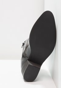Stivaletto in pelle verniciata nera con tacco basso e testurizzato, zip laterale e punta arrotondata liscia, posizionato su uno sfondo neutro.
