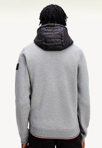 Grå sweatshirt med sort quiltet hætte, ribbede manchetter og kant, med en sidelomme og en lille logopatch på ærmet.