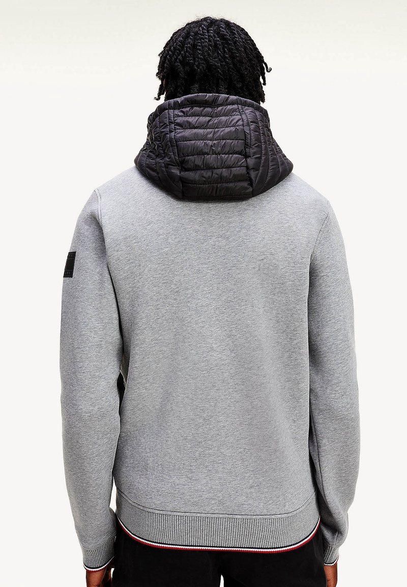 Grå sweatshirt med sort quiltet hætte, ribbede manchetter og kant, med en sidelomme og en lille logopatch på ærmet.