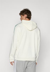 Cream hoodie with a drawstring hood, featuring turquoise stripes along the shoulders and ribbed cuffs. Soft texture.