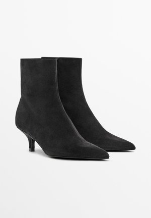 Schwarze Wildleder-Stiefeletten mit spitzen Zehen und Kittenheels. Glatte Textur, minimalistisches Design mit einer strukturierten Silhouette.