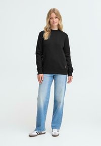 Felpa nera con collo a giro, maniche lunghe e polsini a coste, abbinata a jeans a gamba dritta blu chiaro e sneaker bianche con righe nere.