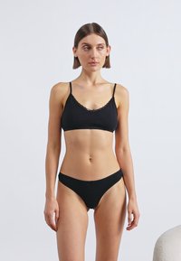 Σετ μαύρα εσώρουχα που περιλαμβάνει σουτιέν με ρυθμιζόμενους ιμάντες και δαντέλα στο τελείωμα, σε συνδυασμό με μπικίνι κάτω μέρος χαμηλής μέσης. Ομαλή υφή υφάσματος.