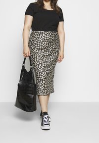 Svart topp med korta ärmar kombinerad med en knälång svart kjol med blommönster. Accessoarer inkluderar en stor svart tygväska och svarta sneakers.