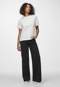Weißes Baumwoll-T-Shirt mit kurzen Ärmeln, kombiniert mit weit geschnittenen schwarzen Jeans aus Denim. Die Jeans haben eine hohe Taille und einen subtilen Verblassungsgrad.