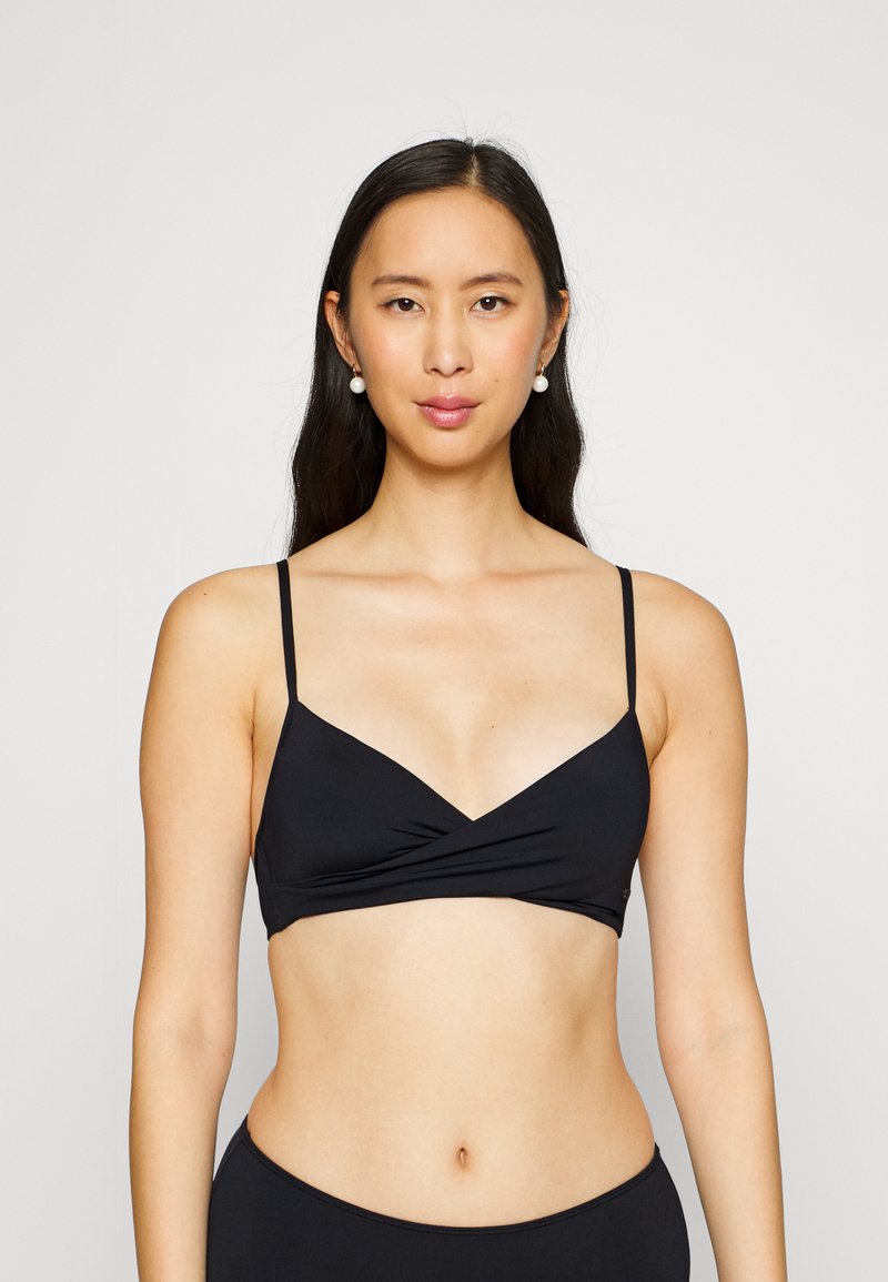 Zwarte bralette met dunne verstelbare bandjes, driehoekige cups en een gedraaide voorkant. Gladde stof met minimale hardware.