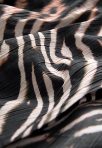 Schwarzer und beiger Stoff mit wellenförmigen Streifen und strukturierter Oberfläche. Das Muster ist flüssig und abstrakt gestaltet mit variierenden Breiten.