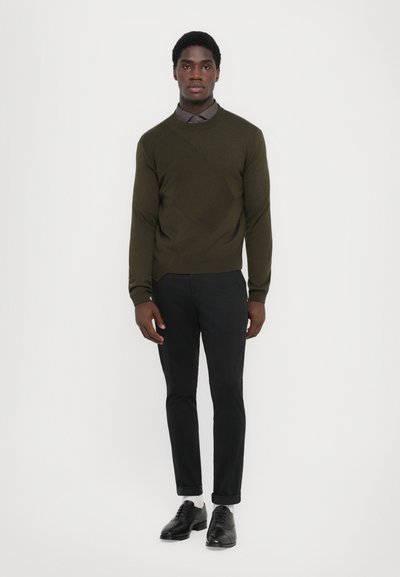 Maglione verde scuro con un motivo testurizzato, pantaloni neri slim-fit e scarpe nere. L'outfit presenta una camicia con colletto sotto.