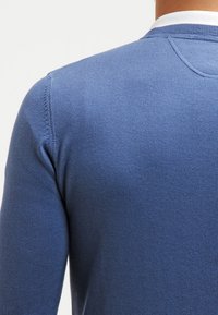 Blauer Strickpullover mit langen Ärmeln, Rundhalsausschnitt, strukturiertem Stoff und kontrastierendem weißen Kragenrand. Ausführliche Stickereien auf den Schultern.