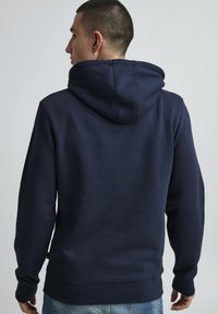 Felpa con cappuccio blu navy, materiale misto cotone, texture morbida, tasca singola frontale, polsini e fondo a coste, design minimalista.