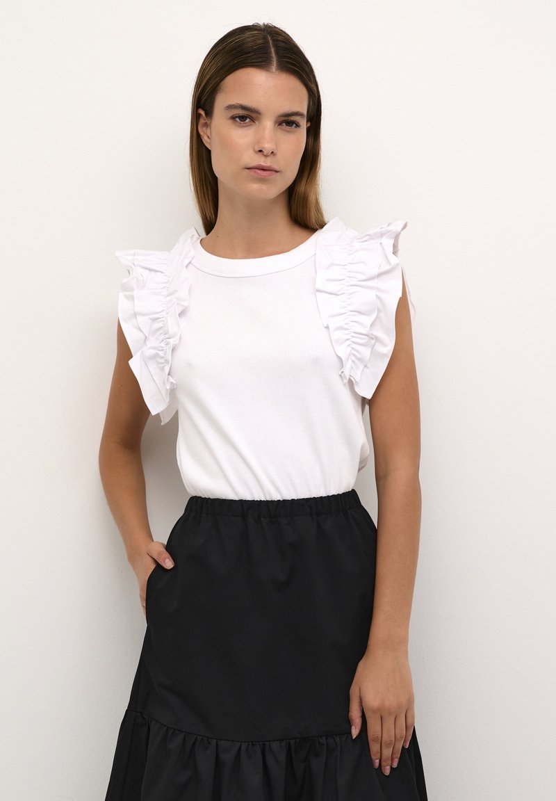 Top bianco senza maniche con design a rouches; abbinato a una gonna nera con vita elastica e orlo a strati arricciato.