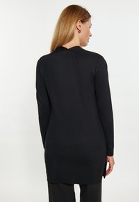 Tunic nera lunga in maglia con maniche lunghe, caratterizzata da spacchi laterali e un collo arrotondato. Tessuto testurizzato con una finitura liscia.