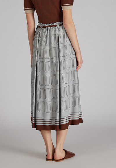 Jupe grise à motifs avec des designs rectangulaires et un ourlet marron. Taille élastique pour un ajustement décontracté. Portée avec des chaussures plates marron à enfiler.