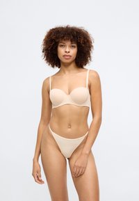 Soutien-gorge en beige avec armatures moulées et bretelles ajustables, texture lisse, et string sans couture assorti. Les deux présentent un design minimaliste.
