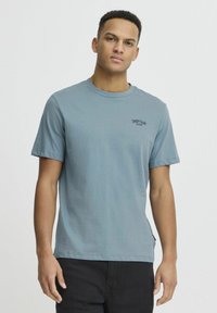 Blå bomulds t-shirt med rund hals, korte ærmer og et lille sort broderet logo på brystet. Glat tekstur, afslappet pasform.