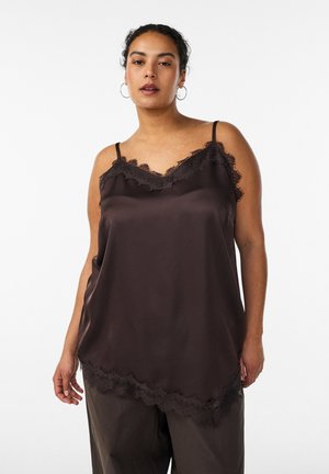 Žena v tmavohnedom saténovom nátelníku s čipkovou lemovkou a širokými hnedými nohavicami na bielom pozadí.
