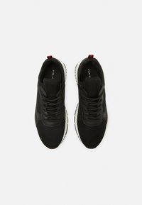 Chaussures de sport noires avec une tige en mesh, une semelle en caoutchouc et une semelle intermédiaire blanche contrastante. Elles comportent des lacets, un col rembourré et un accent rouge au talon.