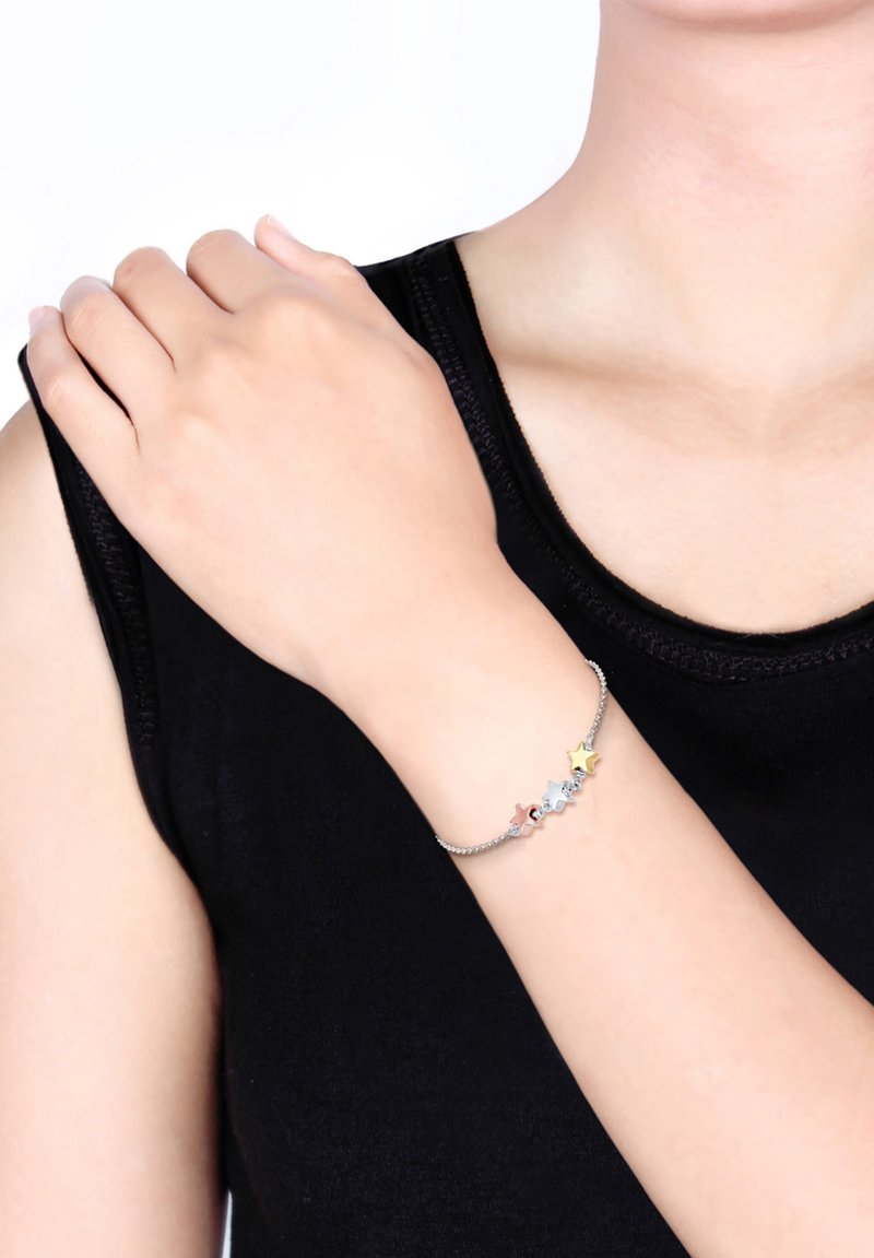 Silverfärgad kedjearmband med färgglada stjärncharms i gult, blått och rosa. Bakgrunden är neutral och presentationen framhäver armbandets design.