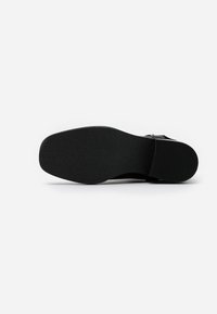 Semelle de chaussure noire en matériau caoutchouteux texturé, forme arrondie, légère hauteur de talon et finition lisse. Présente un design minimaliste sans logos visibles.