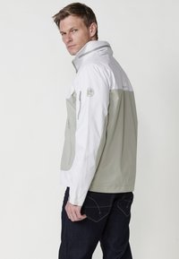 Veste légère et imperméable avec un schéma de couleurs gris et blanc. Dotée d'un col haut, de poches zippées et d'un design moderne et ajusté.