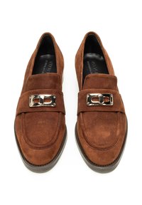 Mocassini in suede marrone con una larga fascia e dettagli con fibbia metallica; punta arrotondata; suola piatta; superficie liscia e texture.
