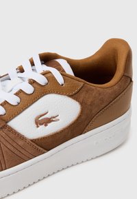 Braune Leder- und Wildledersneaker mit weißen Akzenten, strukturierten Paneelen, runden weißen Schnürsenkeln und einem kleinen Krokodillogo an der Seite.