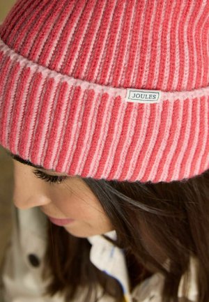 Frau mit einer rosa-rot gestreiften Strickmütze mit der Aufschrift "Joules", die nach unten blickt, wobei ihr langes dunkles Haar sichtbar ist.