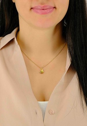 Collier en or avec un petit pendentif décoratif, porté sur un chemisier beige clair. La chaîne est délicate et présente une finition polie.