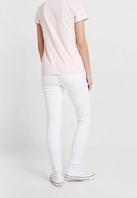 Jasnoróżowa koszulka z krótkim rękawem w połączeniu z białymi rurkami i białymi trampkami. Ubranie charakteryzuje się prostym wzornictwem i dopasowanym krojem.