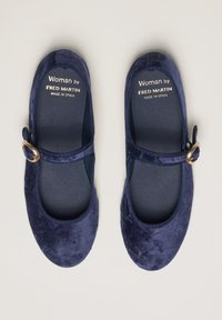 Bailarinas de terciopelo azul marino con punta redonda, tira elástica y detalle de hebilla dorada. Cuenta con un suave forro interior y suela texturizada.