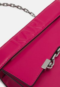 Różowa skórzana torebka z łańcuszkowym paskiem, płaską klapą, wytłoczonym logo "KARL" oraz srebrnymi akcentami.