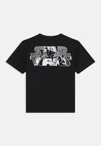 Svart t-skjorte med korte ermer og stor hvit konturert "Star Wars"-tekst på ryggen, med et stilisert grafisk bilde av Darth Vader inni bokstavene.