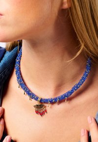 Collier tressé en perles bleues avec des accents dorés, comportant un charme en forme d'éventail et des perles rouges. Design texturé avec des détails dorés pendants.