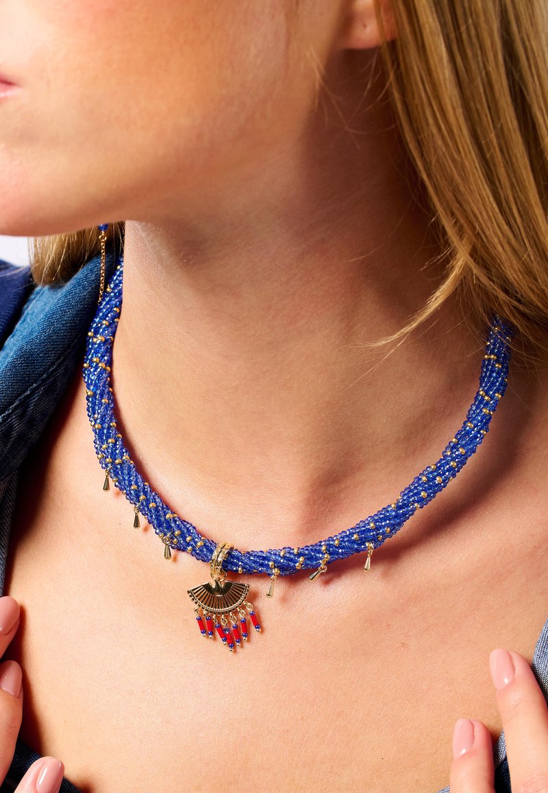 Collier tressé en perles bleues avec des accents dorés, comportant un charme en forme d'éventail et des perles rouges. Design texturé avec des détails dorés pendants.