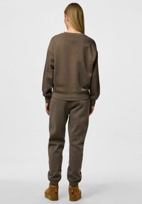 Felpa marrone e joggers abbinati realizzati in un tessuto morbido; presentano polsini elasticizzati e una vestibilità rilassata, abbinati a calzature in texture tan.