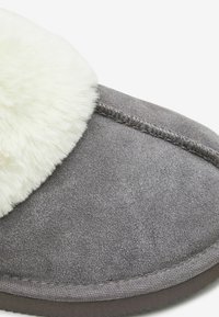 Chausson gris avec un doux bord en fourrure blanche, dessus en daim, forme arrondie et détails de couture contrastants le long des bords. Semelle plate.