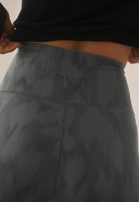 Gray high-waisted leggings with a subtle textured pattern, featuring a logo at the waistband and contrasting flatlock seams.