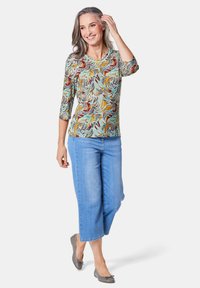 Patronen top met driekwartmouwen in lichtblauw, voorzien van spiralen in oranje, rood en groen; gecombineerd met cropped denim broek en grijze flats.
