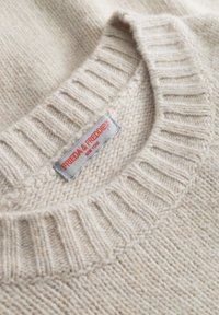 Beige gebreide trui met een geribde halslijn en een label met de tekst "FREDA & FREDDIES." Zachte textuur en geweven patroon zichtbaar in de stof.