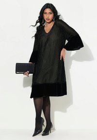 Schwarzes Kleid mit strukturiertem Muster, ausgestellten Ärmeln und samtigen Akzenten. Kombiniert mit schwarzen High Heels und einer passenden Clutch.