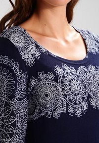 Marineblaues Sweatshirt mit aufwendiger weißer Spitzenstickerei entlang des Ausschnitts und der oberen Brust, mit floralen und kreisförmigen Mustern.