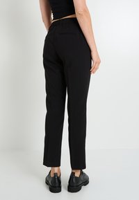 Pantalones elásticos negros de corte slim, con cinturilla elástica y dos bolsillos traseros. El material tiene una textura suave y un corte recto.